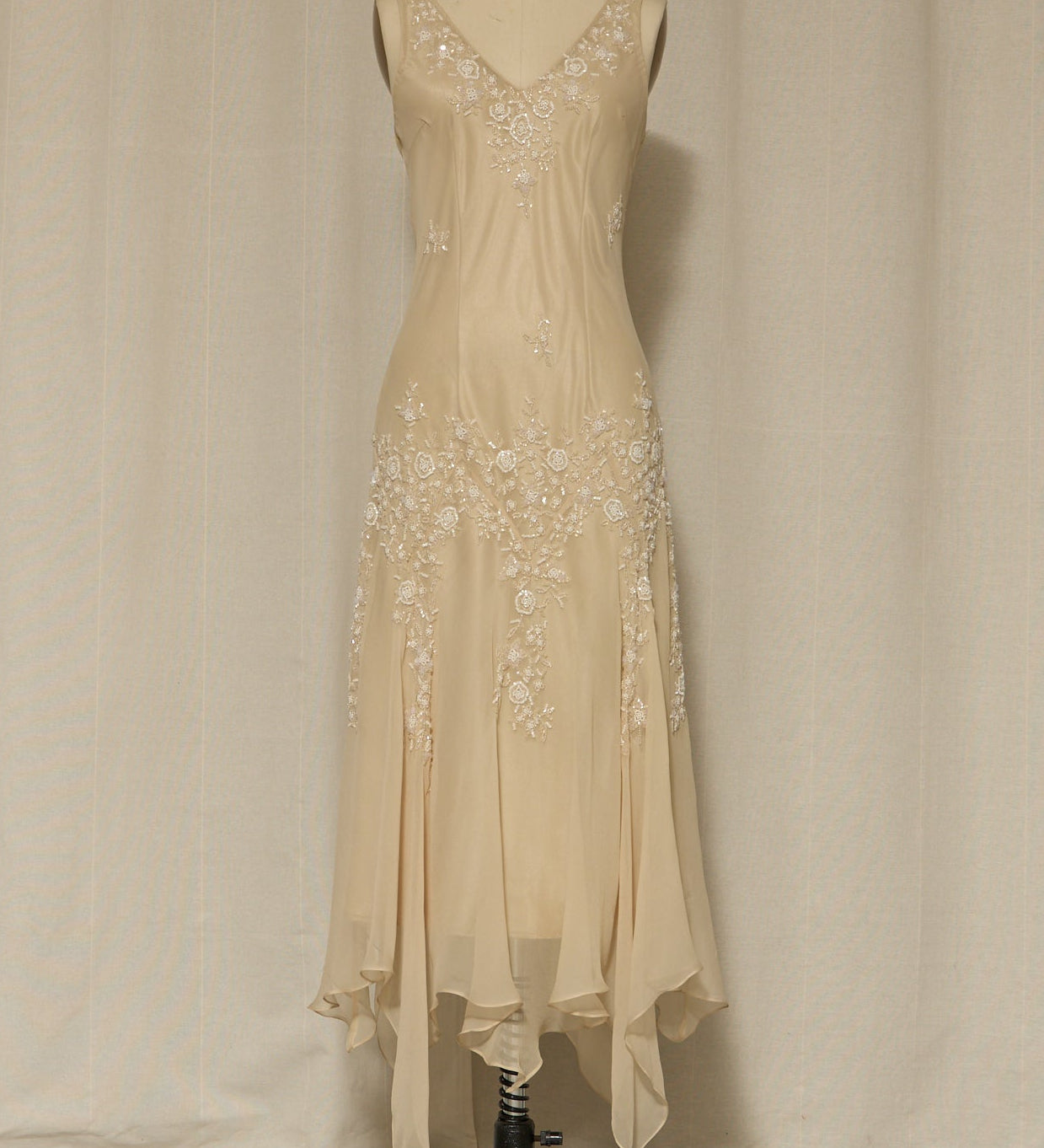 Beige evening gown with floral embellishments on a mannequin against a plain background