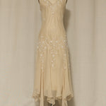 Beige evening gown with floral embellishments on a mannequin against a plain background