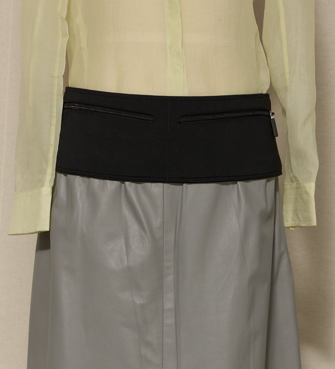 Light green shirt over gray skirt with black waistband on a beige background
