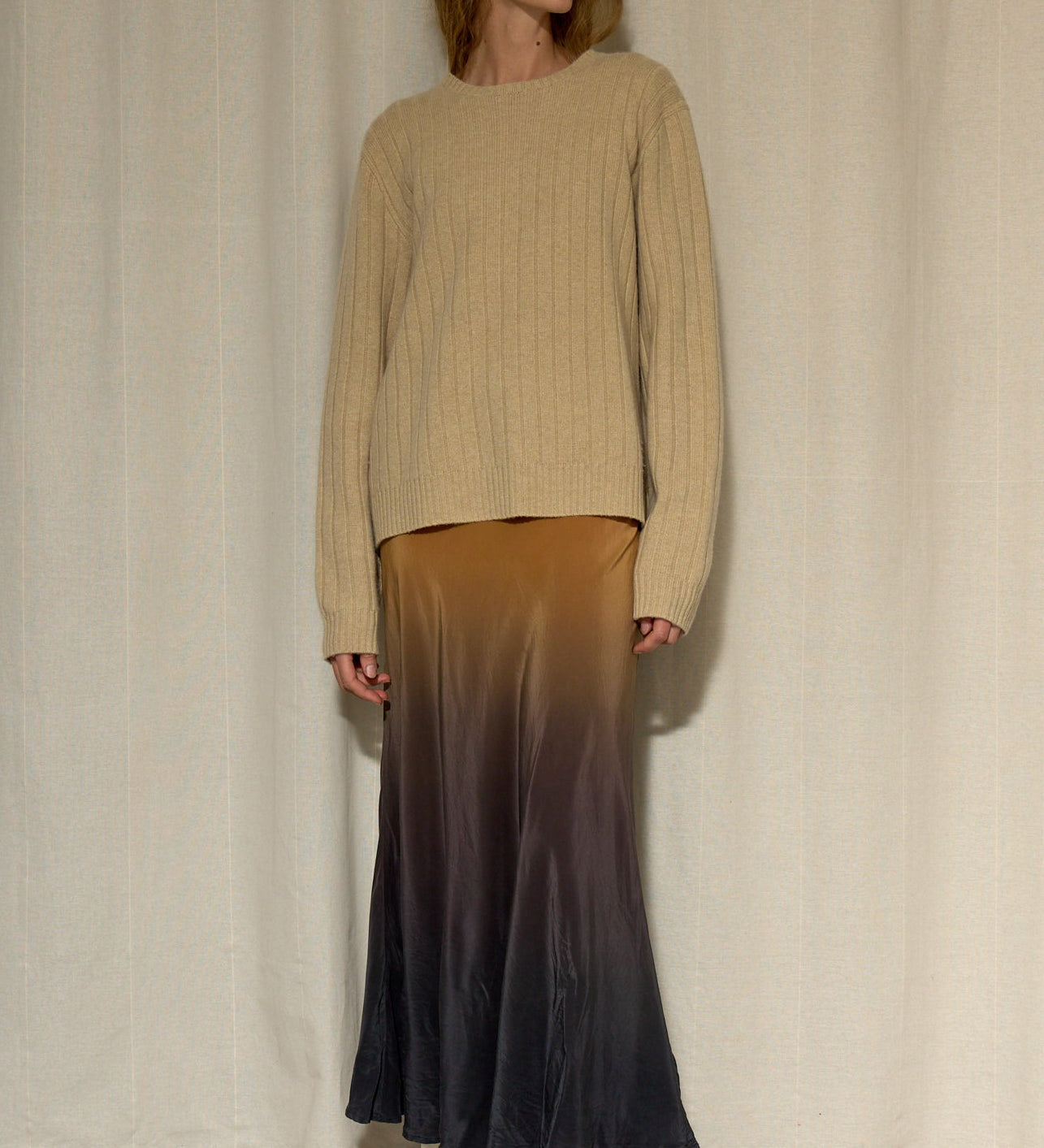 Woman wearing a beige sweater and gradient skirt against a plain background