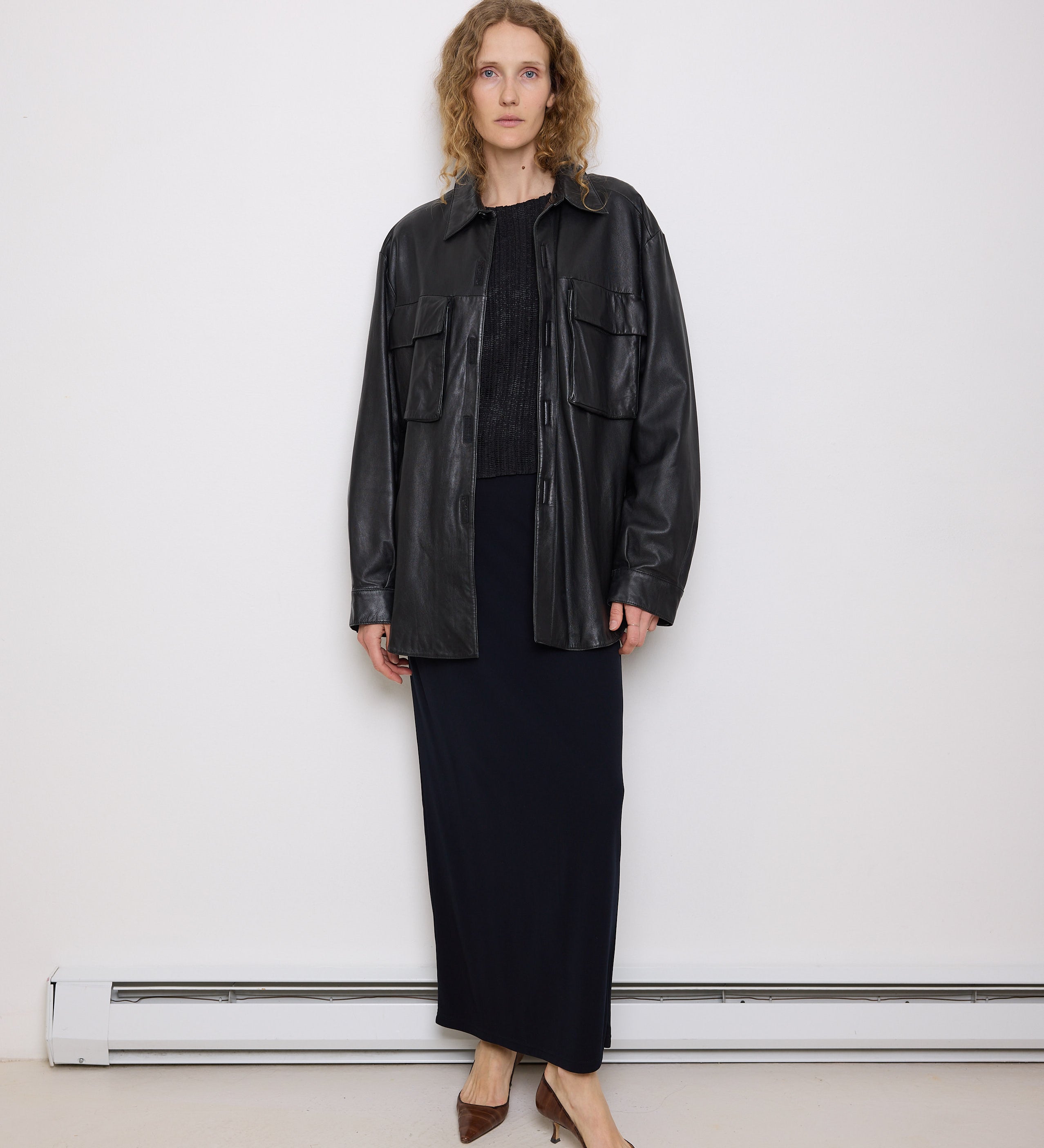 Oversized vintage black leather utility jacket with flap chest pockets, worn by model over black skirt.