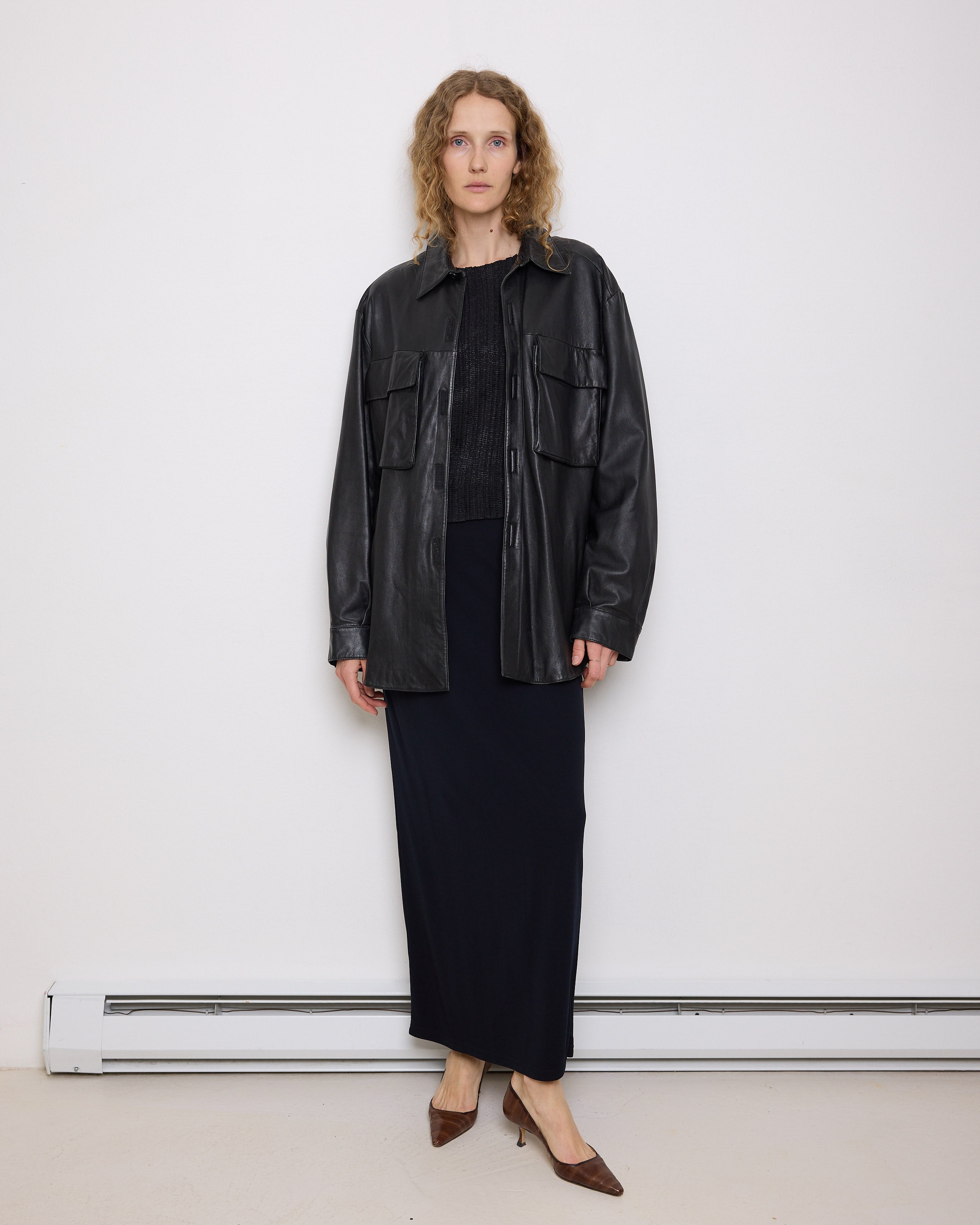 Oversized vintage black leather utility jacket with flap chest pockets, worn by model over black skirt.
