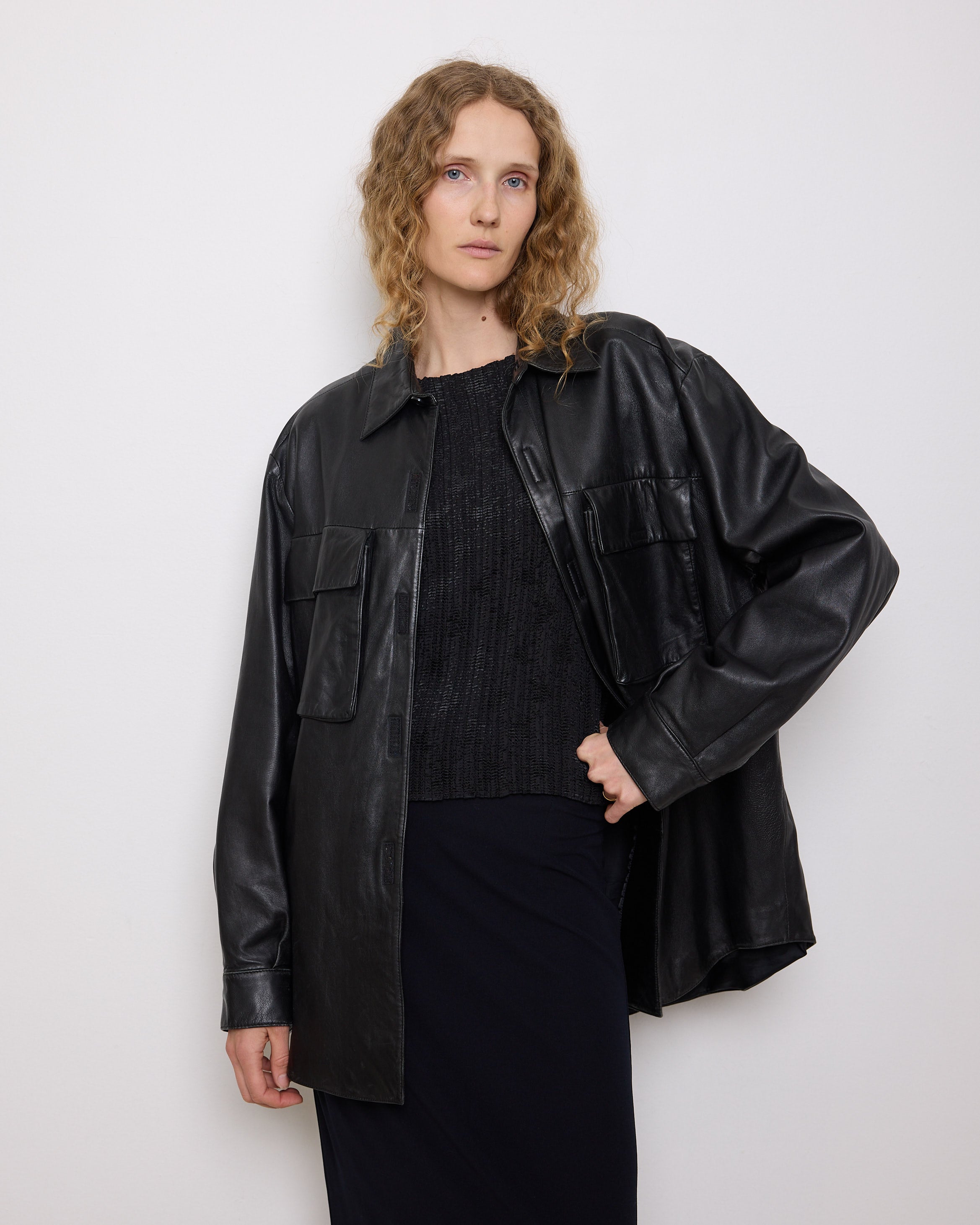 Oversized vintage black leather utility jacket with flap chest pockets, worn by model over black skirt.