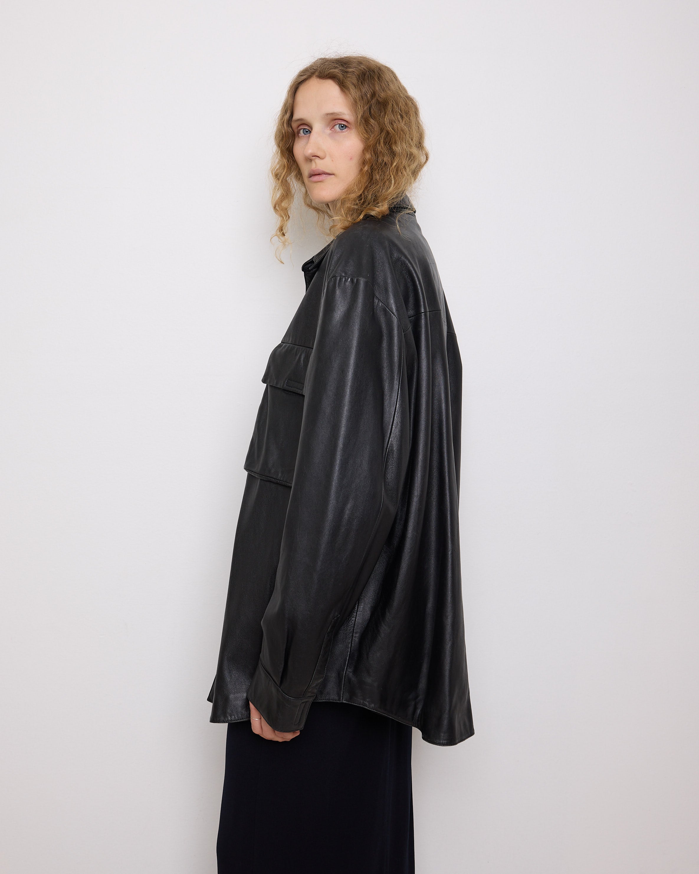Oversized vintage black leather utility jacket with flap chest pockets, worn by model over black skirt.