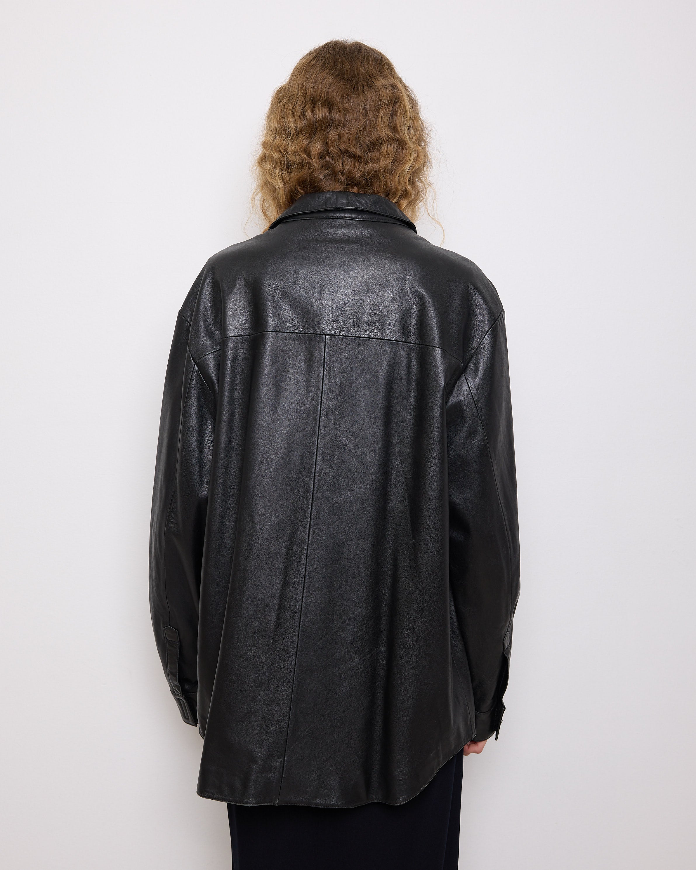 Oversized vintage black leather utility jacket with flap chest pockets, worn by model over black skirt.
