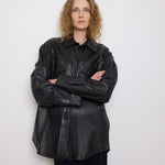 Oversized vintage black leather utility jacket with flap chest pockets, worn by model over black skirt.